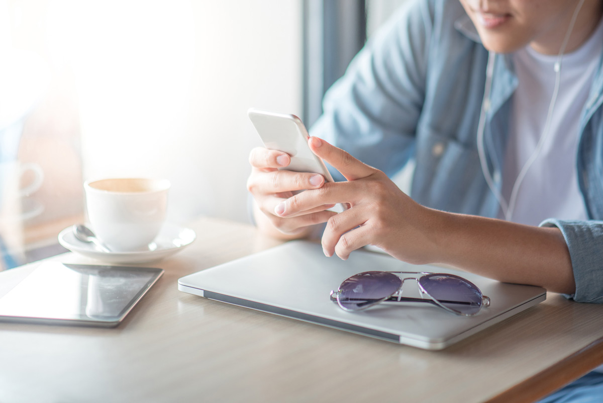 contact-us Photo of a man sitting at a desk with a laptop, phone, and a cup of coffee, using phone to message