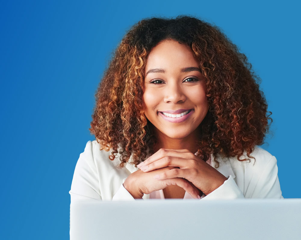 otr-sub-hero-mobile Photo of a woman with laptop, notepad and coffee cup, sitting against a blue background.